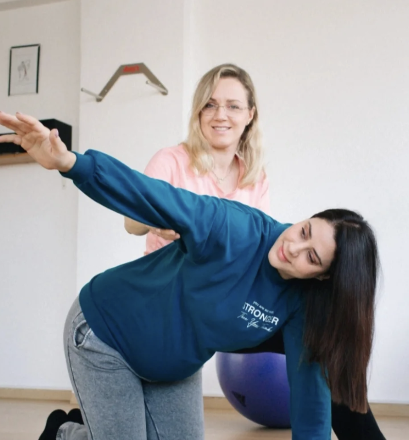 Certified Pelvic Floor Physiotherapist guiding a postpartum mother through a core recovery exercise on a Pilates ball